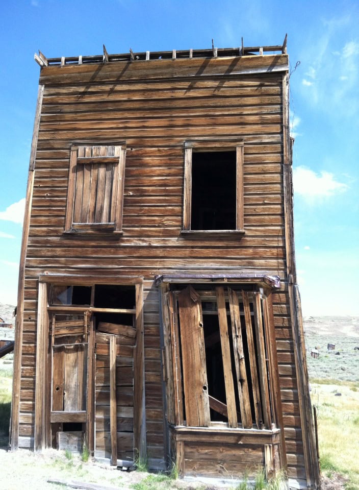 Decaying wooden abandoned building with broken windows and weathered exterior, under a clear blue sky.