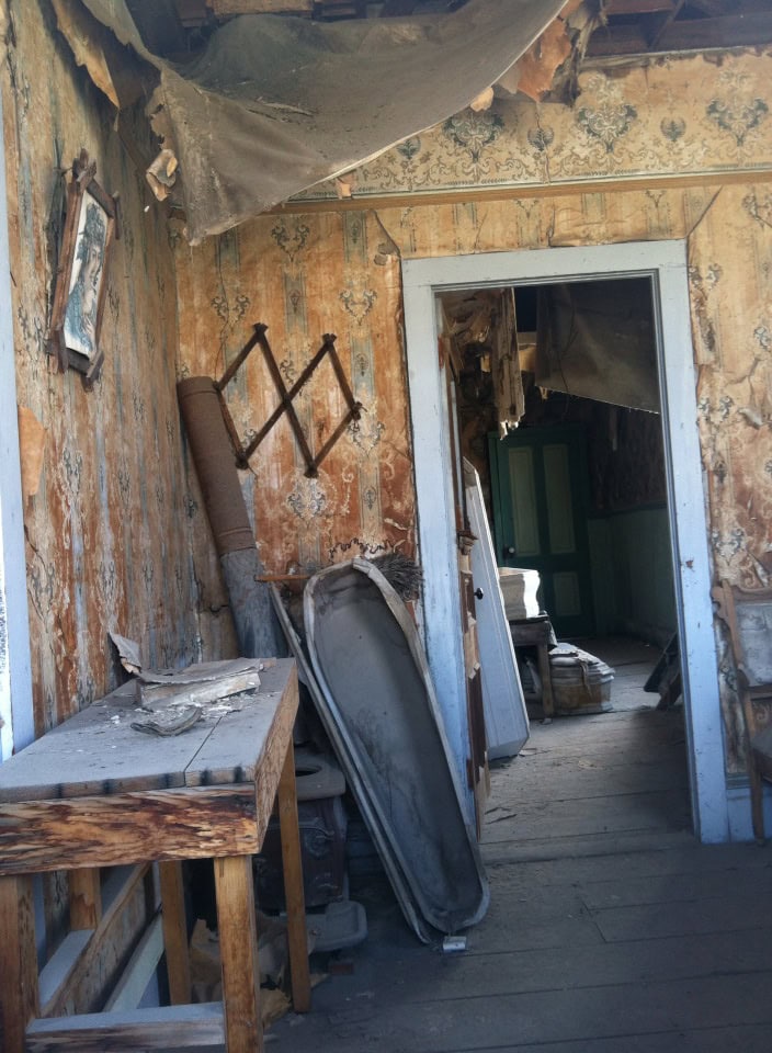 Rustic abandoned interior with peeling wallpaper, old furniture, and dust-covered items, creating a nostalgic, vintage atmosphere.