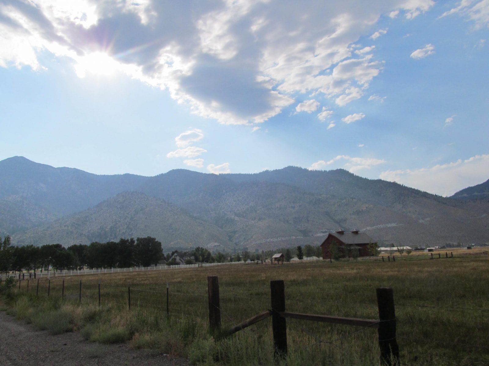 Serene mountain landscape with clear blue sky, fluffy clouds, and rustic barn in a rural setting, perfect for nature lovers and outdoor enthusiasts.