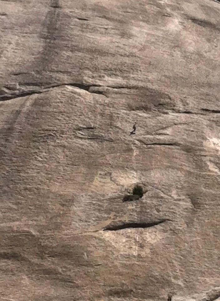Rock face with a tiny climber resembling a face profile, natural rock formations, outdoor adventure, climbing, scenic mountain landscape.