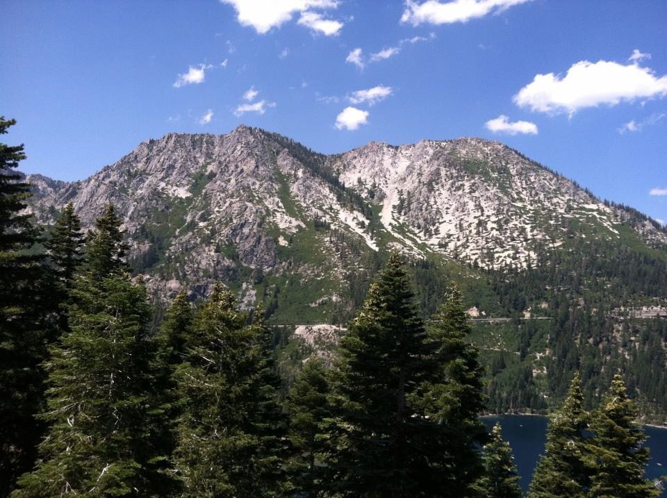 Majestic mountain landscape with lush green trees and a serene lake under a bright blue sky, perfect for outdoor adventures and nature photography.
