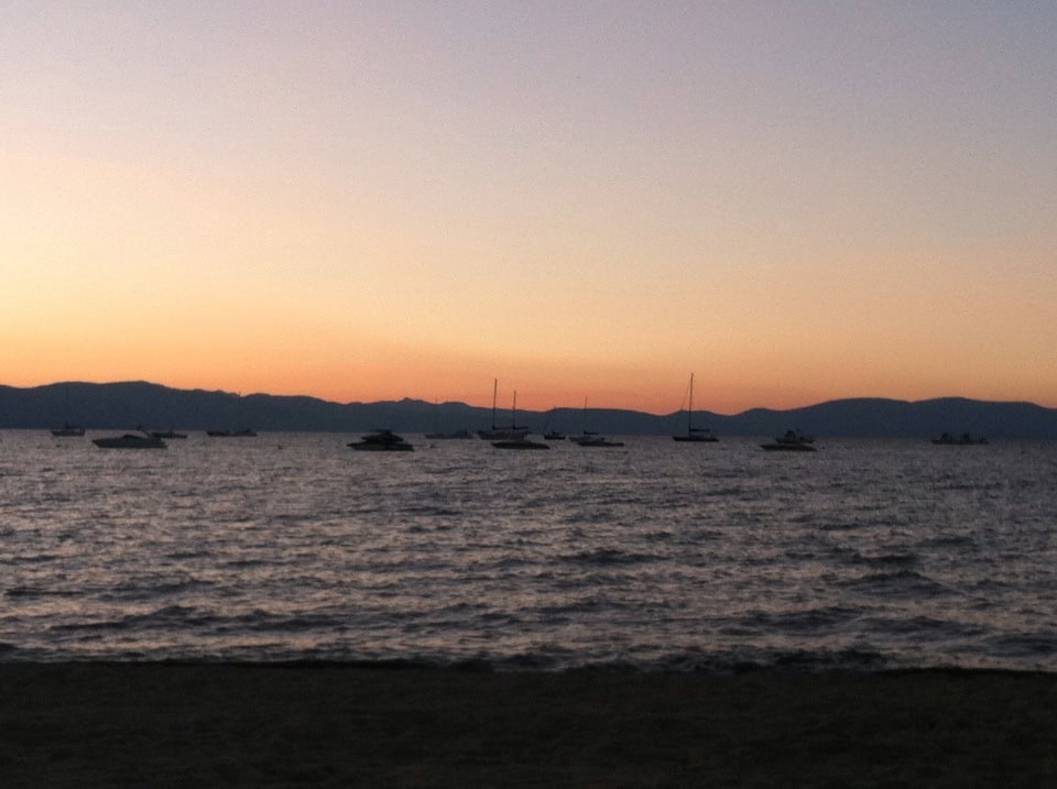 Relaxing lakeside sunset with boats on calm water and distant mountains, perfect for peaceful evening reflections and romantic getaways.