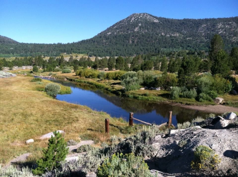Serene mountain landscape with a calm river, lush greenery, and clear blue sky at A Hundred Affections.