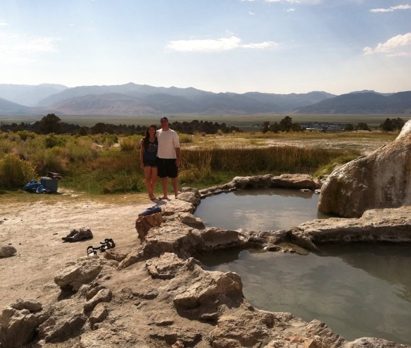 Scenic outdoor hot springs surrounded by mountains with a couple enjoying the natural setting, perfect for relaxation and connecting with nature.