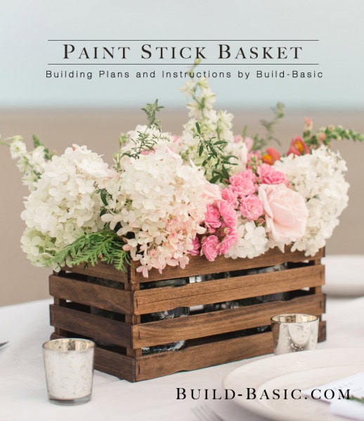 Colorful paint stick basket filled with pink and white flowers, rustic wooden planter for DIY floral arrangements, perfect for home decor and craft projects.
