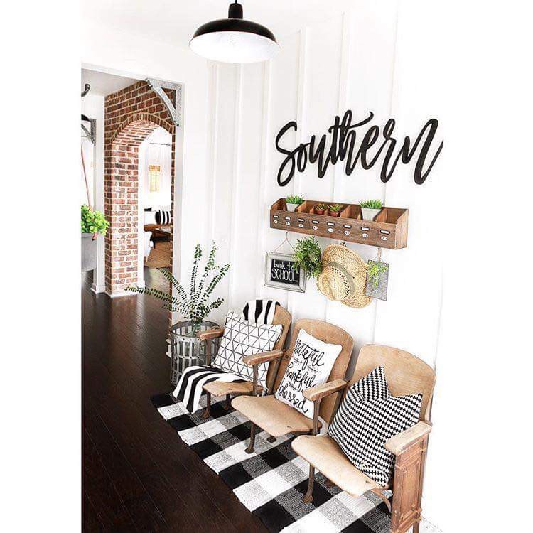 Entryway with chairs, buffalo check rug, black and white pillows, shelf with hooks, flowers, plants, and 'Southern' sign on wall