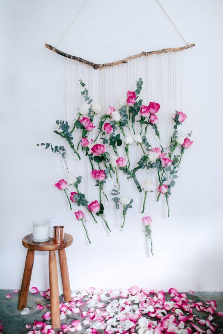 A delicate floral wall hanging with pink and white roses, eucalyptus, and thin strings, creating an elegant, romantic display for home decor or special events.
