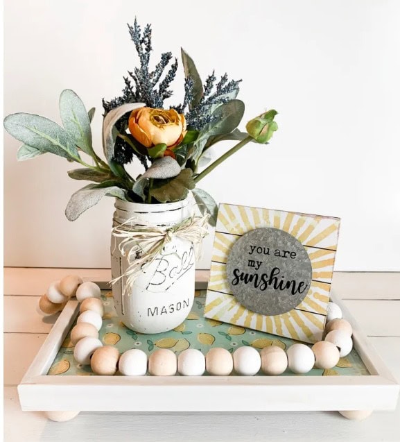 Mason jar floral arrangement with greenery and yellow flower, decorative "you are my sunshine" plaque, wooden bead tray, and pastel decor, perfect for home or gift decor.