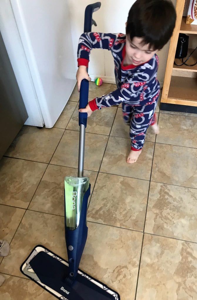 Child vacuuming in pajamas, kitchen cleaning, child chores, toddler helping with household tasks, indoor cleaning activity.