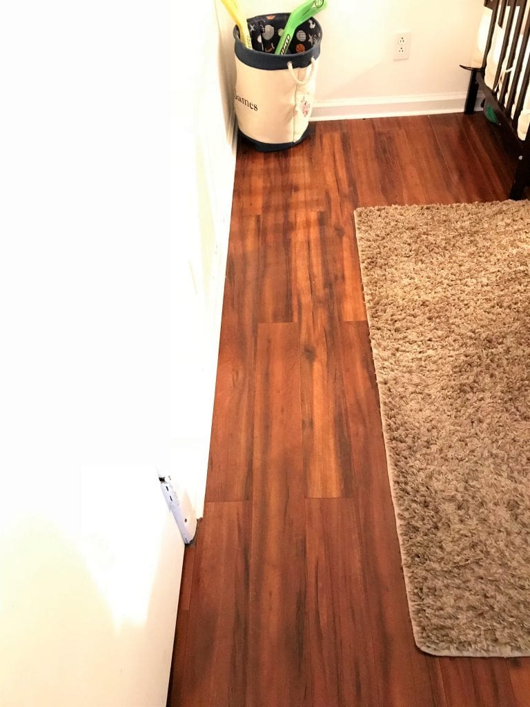 Polished hardwood floor in a cozy nursery or playroom with a beige shag rug, toys, and a crib, emphasizing warm home décor and child-friendly space design.