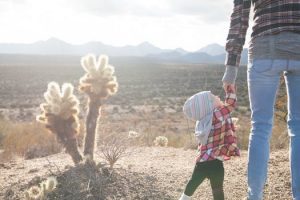 A parent and child holding hands in a desert landscape with cacti and mountains in the distance, symbolizing outdoor family adventures and meaningful moments, perfect for building cherished memories.
