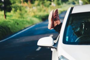 Someone's legs with stylish brown boots hanging out of a car window on a scenic road.