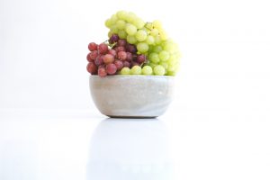 Colorful grapes in a ceramic bowl on a white background.