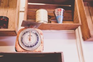 Vintage rusty kitchen scale on wooden shelf with jars and cans in rustic cottage decor.