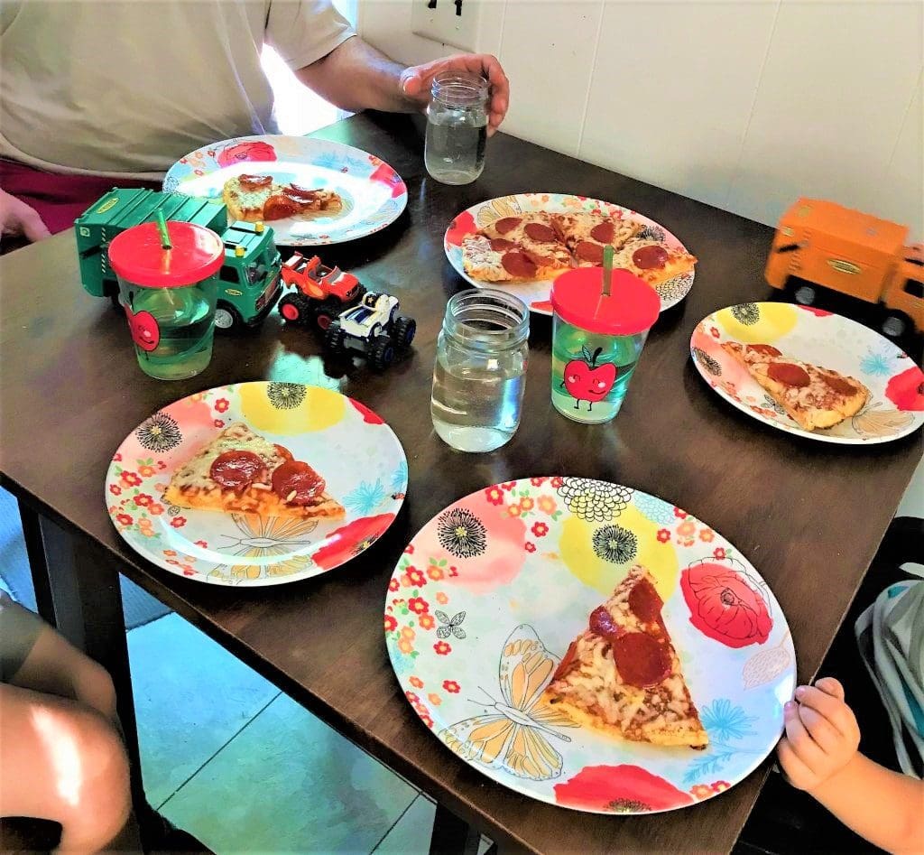 Colorful plates with pizza slices, kid-friendly toys, and water glasses on a dark dining table perfect for family pizza night.