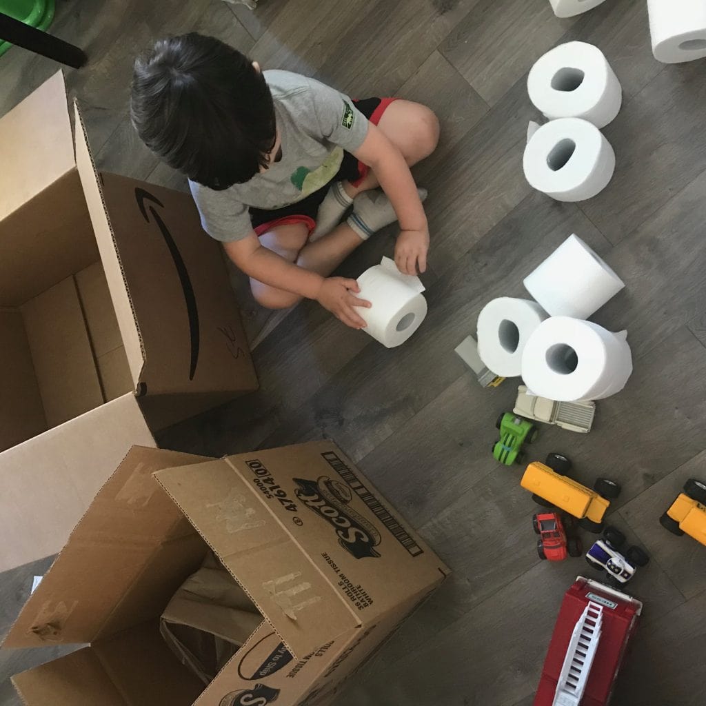Bathroom tissue rolls and toy cars with a child packing boxes for moving.