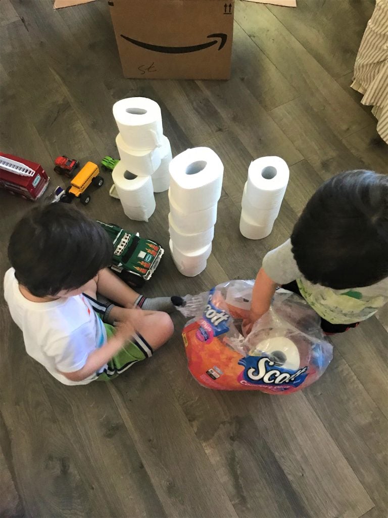 Disorganized children playing with toilet paper and toy cars on wooden floor, indoor setting.