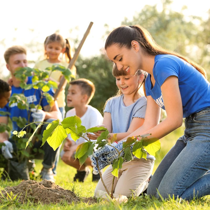 Planting trees with children outdoors, promoting family bonding and environmental awareness. A joyful moment of kids and adults planting and caring for young trees in a sunny park setting.