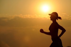 Silhouette of a woman jogging during sunrise on a scenic trail, emphasizing health and fitness, outdoor running, and wellness.