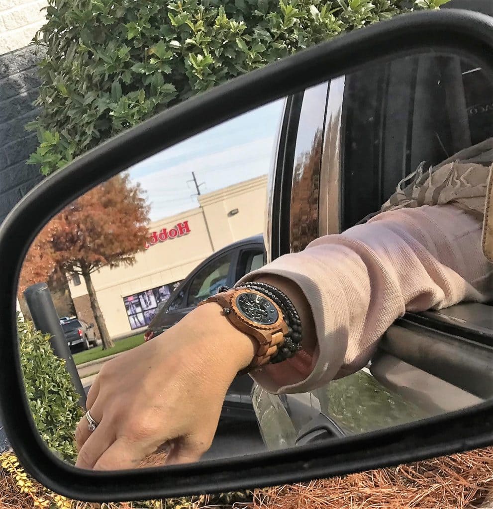 Wooden watch on woman's wrist reflected in side mirror of car.