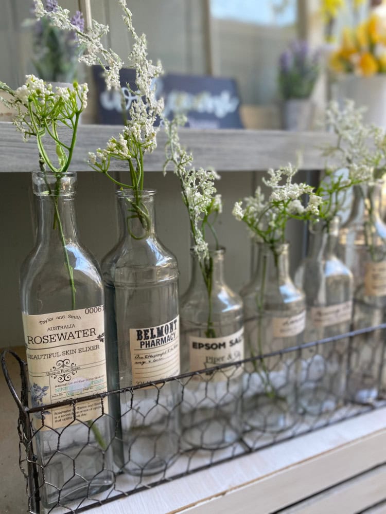 Delicate white baby's breath flowers arranged in vintage glass bottles on a rustic shelf, perfect for shabby chic home decor and floral styling.