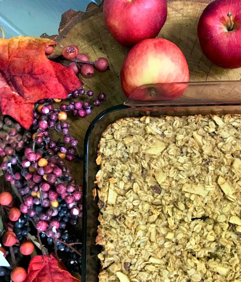 Fresh homemade apple crisp with a crunchy oatmeal topping, surrounded by ripe red apples, fall leaves, and colorful berries. Perfect for cozy autumn desserts.
