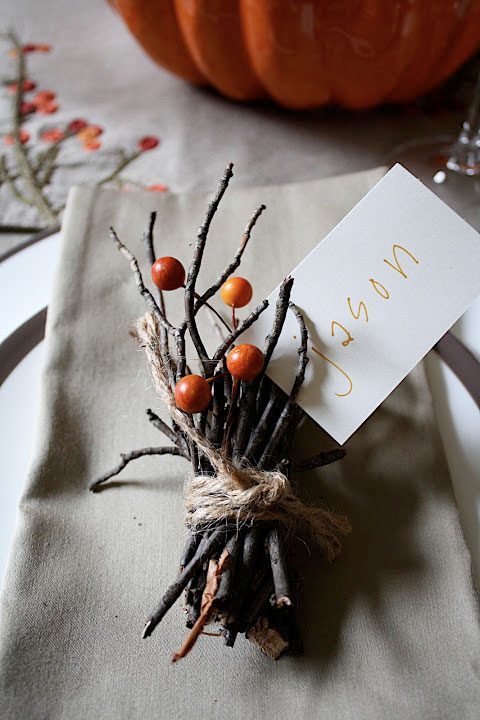 Rustic fall table decor with twig bundle and orange berries, personalized name card for autumn Thanksgiving celebration.