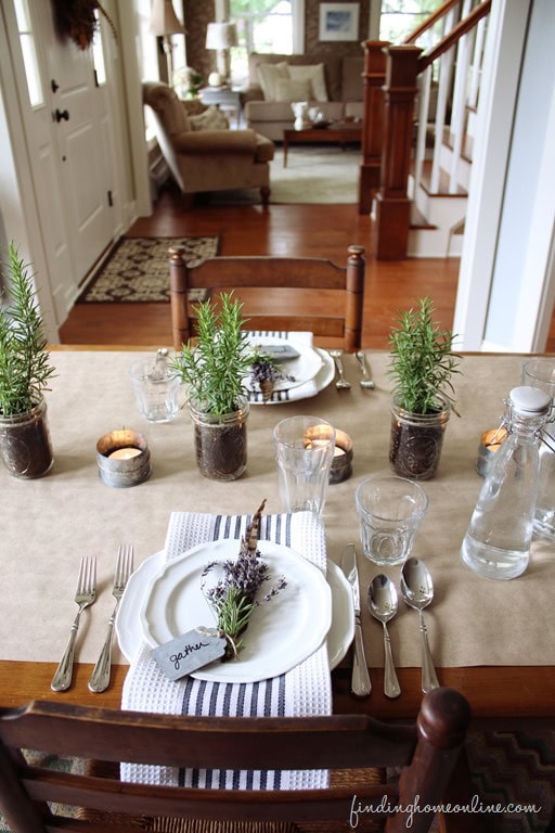 Rustic farmhouse dining table decorated with potted herbs, candles, and elegant tableware for a cozy, inviting home dining experience.