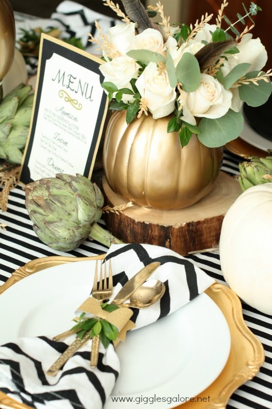 Elegant table setting featuring black and white striped linens, gold cutlery, a floral centerpiece with white roses, and a stylish menu card for wedding or special event decor.