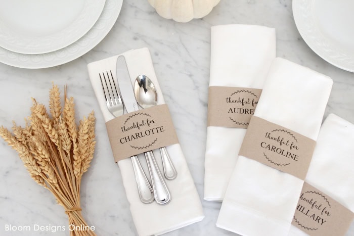 Elegant white napkins with personalized thankful for tags, perfect for wedding or dinner party table settings, styled on a marble surface with a bouquet of dried wheat.