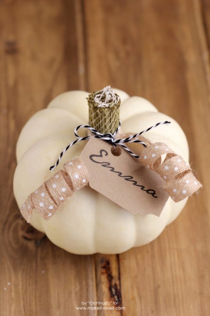 Cream-colored pumpkin with a burlap stem and twine bow, personalized with a kraft paper tag printed with "Elyana," and decorative polka-dotted ribbon for fall decor.