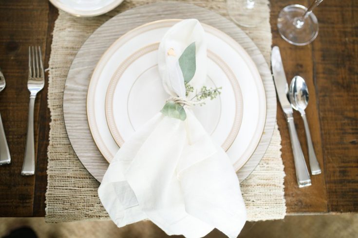 Elegant rustic wedding table setting with white napkin, greenery accents, and vintage-inspired dinnerware, perfect for romantic celebrations and special occasions.
