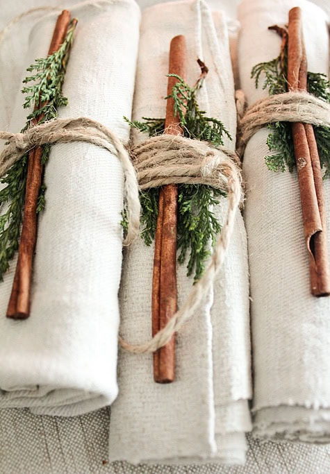 Rustic table setting with cloth napkins, cinnamon sticks, and greenery for holiday or special event decor.