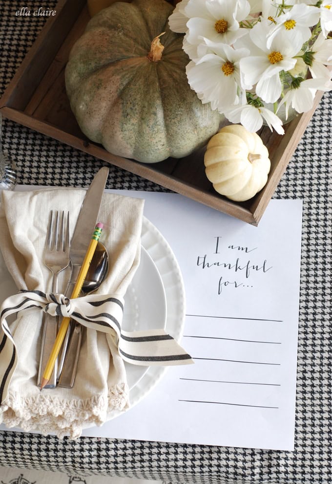 Vase with white flowers and pumpkins on rustic wooden tray, elegant Thanksgiving table setting with thankful note and black and white napkin, fall harvest decor for autumn celebration.
