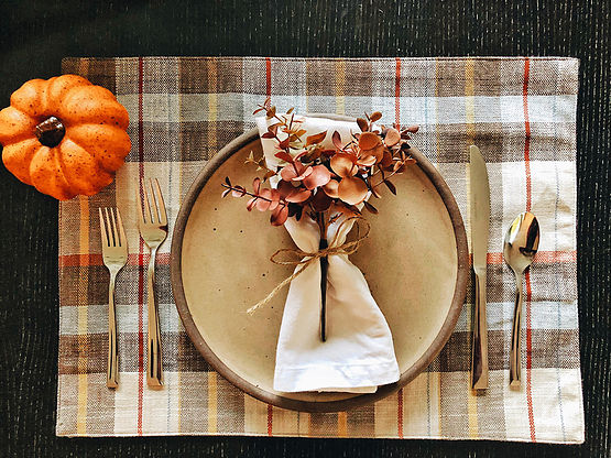 Rustic autumn table setting with a beige ceramic plate, dried pink flowers, and cozy fall decor including a small pumpkin, perfect for Thanksgiving or fall gatherings.