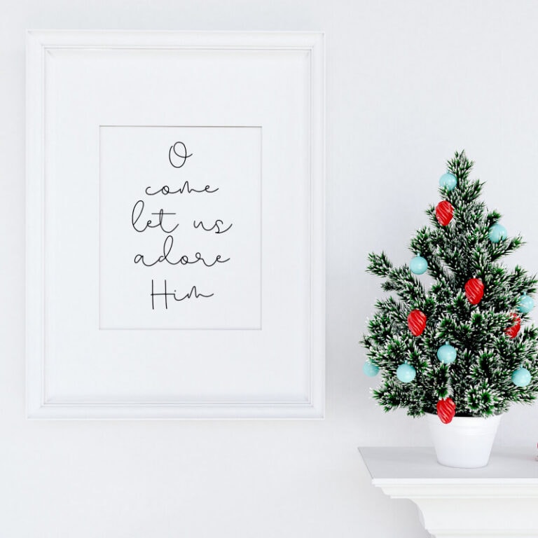 Festive Christmas decor with a decorated snowy pine tree and minimalist wall art reading "O come let us adore Him" at A Hundred Affections.