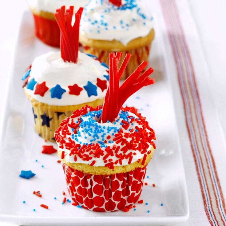 Colorful Fourth of July themed cupcakes with red white and blue sprinkles and decorations on a white tray - perfect for patriotic celebrations and baking ideas.
