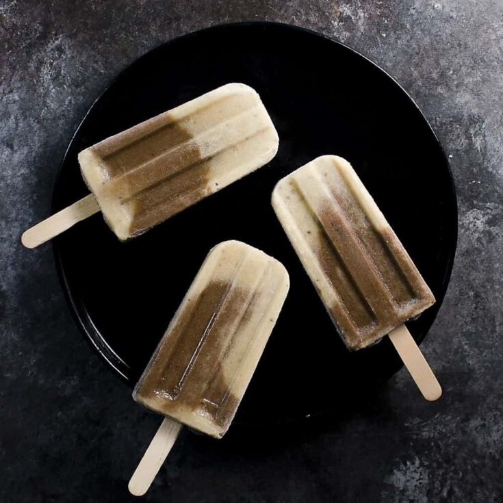Creamy homemade vanilla and chocolate swirl popsicles on a black plate, perfect summer treat for kids and adults.