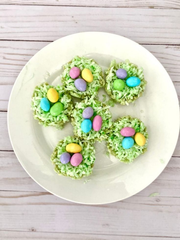 Colorful Easter coconut haystack cookies decorated with pastel candy eggs on a white plate for spring holidays.