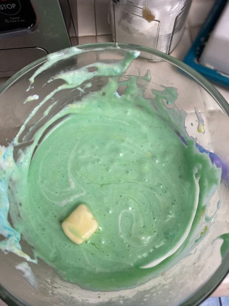Vibrant green melting chocolate in glass mixing bowl, ideal for creative dessert decoration or baking projects, with a small piece of white chocolate on top.