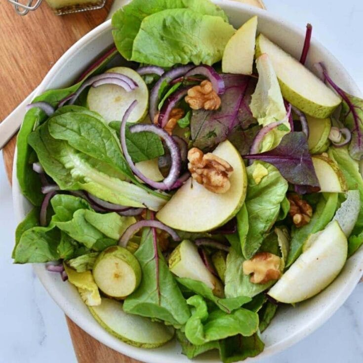 Fresh mixed green salad with apples, walnuts, and red onion, served in a white ceramic bowl for healthy eating and wellness.