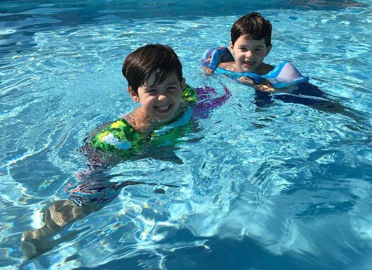 Smiling boys swimming in a clear blue pool, enjoying summer fun, kids swimming safety, outdoor water activities, family-friendly swimming lessons and aquatic play.