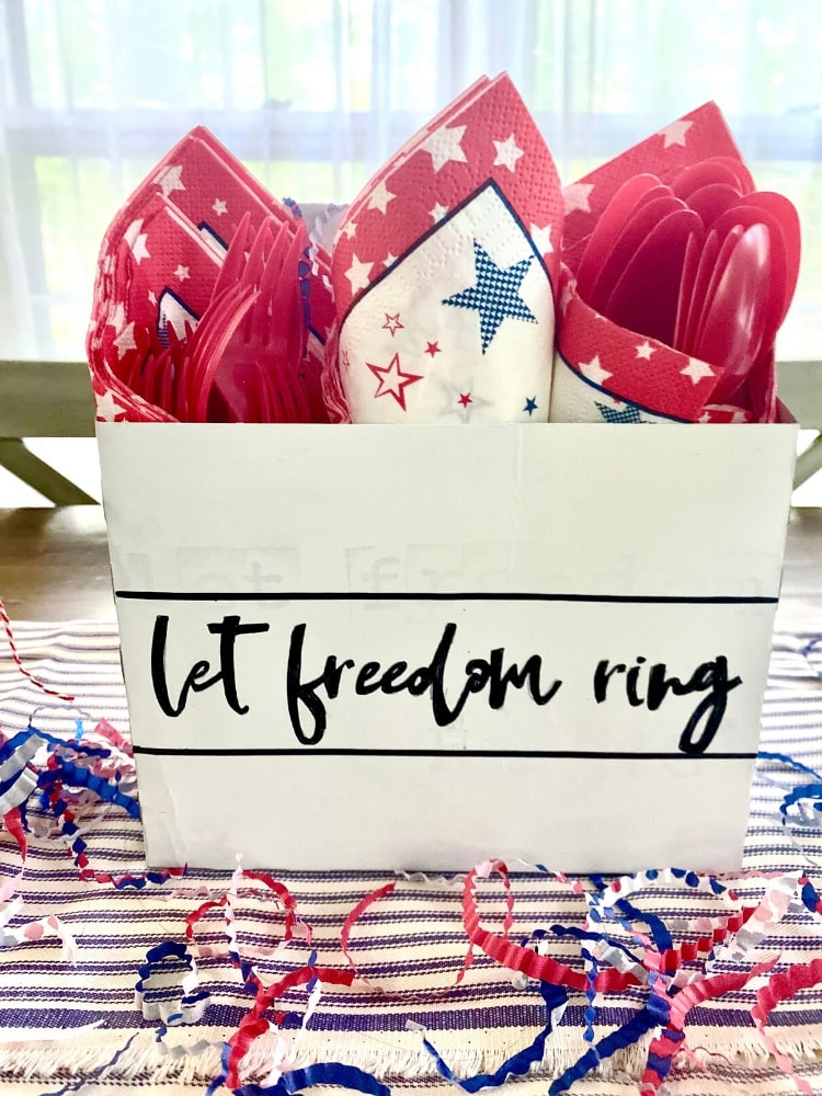 Red, white, and blue patriotic napkins with star patterns in a white box displaying "Let freedom ring" in black text, surrounded by colorful confetti and streamers.