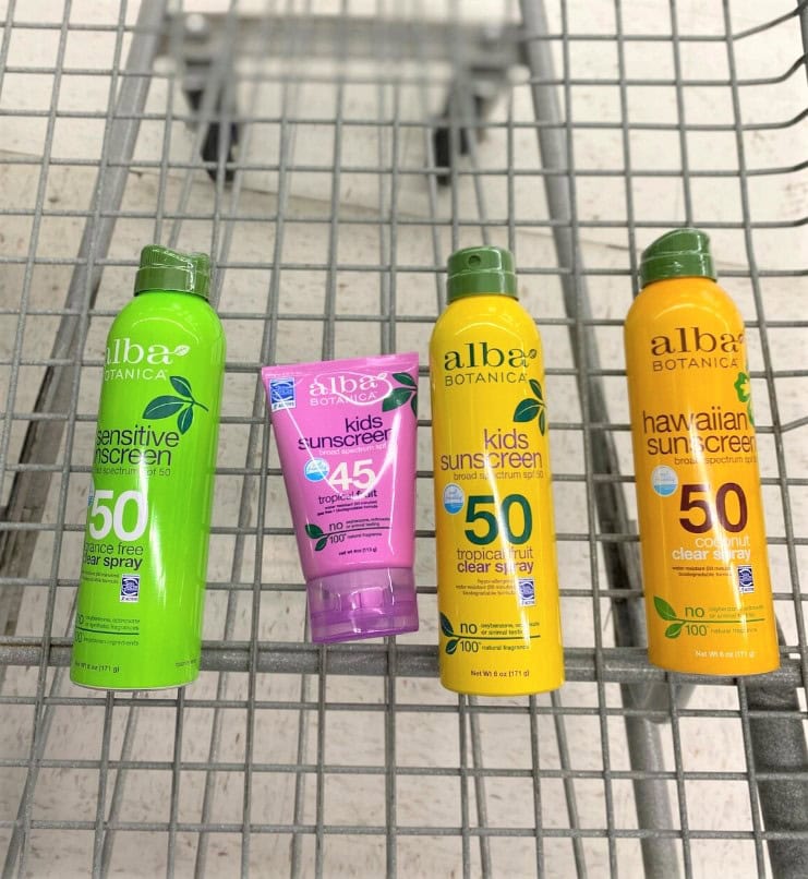 Brightly colored Alba Botanica SPF sunscreens and kids sunblock spray on a shopping cart for outdoor sun protection.