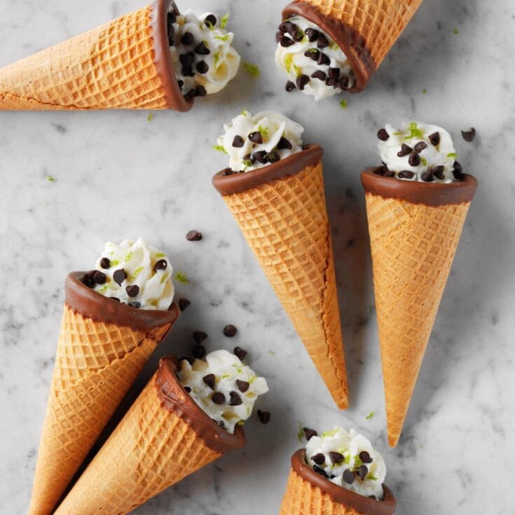 Cream-filled waffle cones topped with chocolate and sprinkled with chocolate chips and lime zest, perfect for a sweet treat or ice cream dessert.