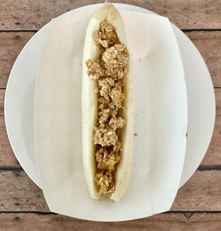sliced banana in tray filled with granola, for clean banana split boat