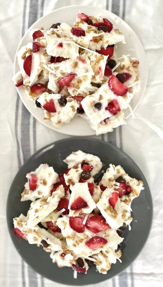 Delicious white chocolate bark with dried strawberries and chocolate chips on white and black plates, perfect Valentine's Day treat or gift.