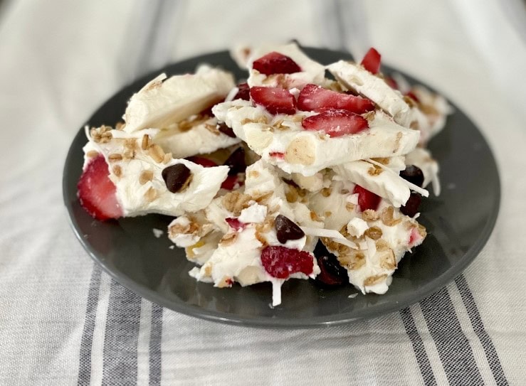 Colorful homemade peppermint bark with berries and chopped nuts on a black plate.