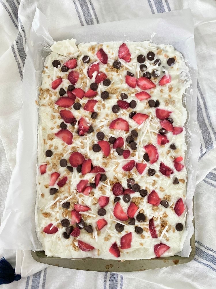 Fresh strawberry and chocolate chip fruit pizza with coconut flakes on a white creamy base, served on a baking sheet.
