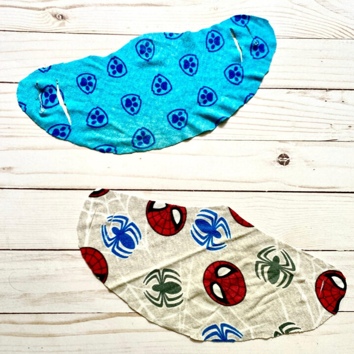 Blue patterned cloth face mask with paw print design, laid on light wood surface.